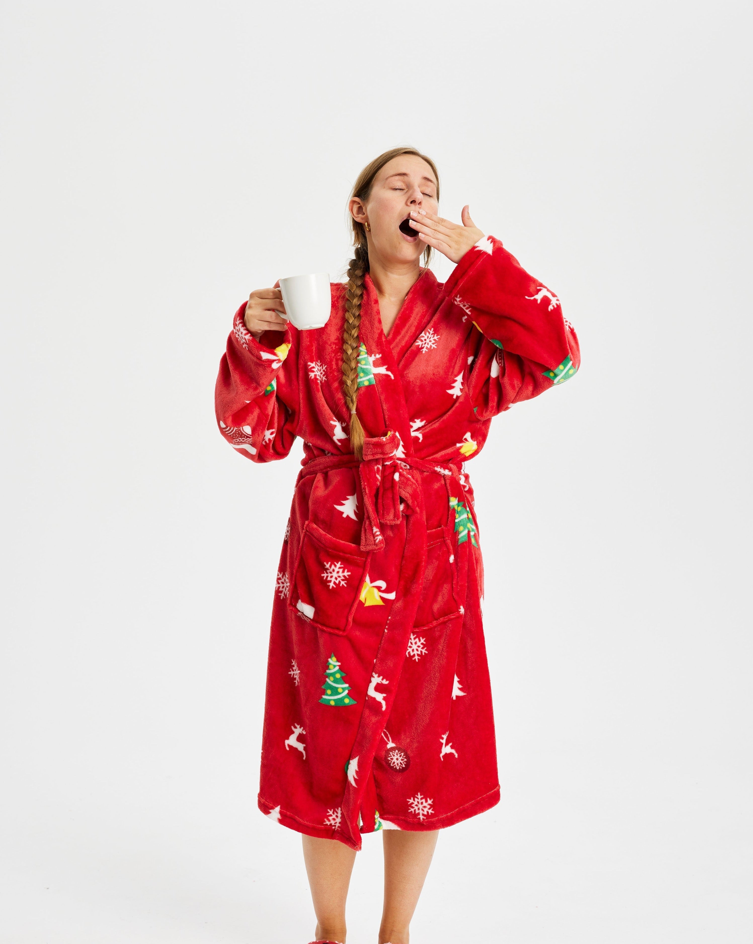 Eine gähnende Frau in einem roten Weihnachtsbademantel mit Weihnachtsmotiv.