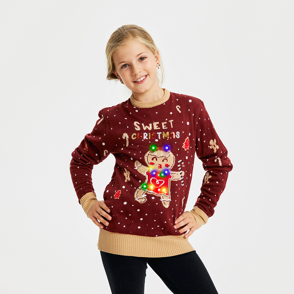 Et smilende barn iført en julesweater i rød med en kagekone, der danser og lyser.